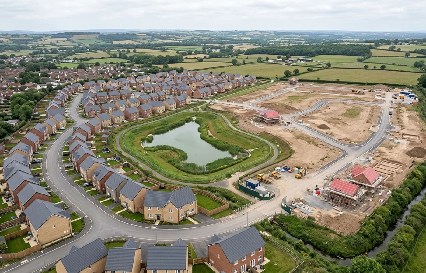 An aerial view of a large housing urban extension on the edge of a Devon town, part built, with completed streets on one side and graded plots on the other